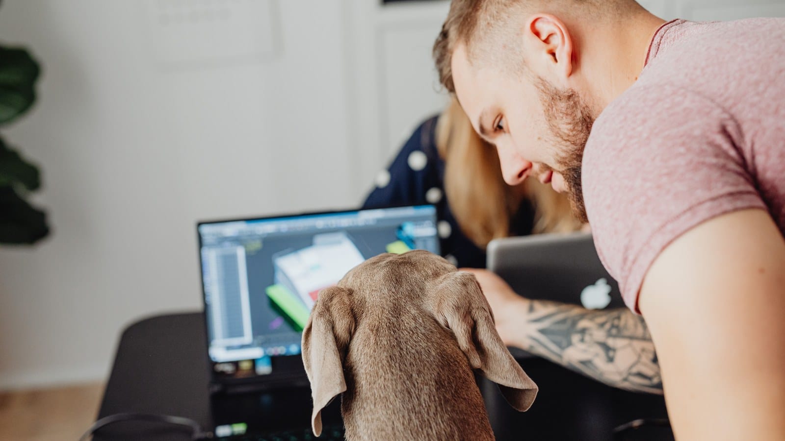 A man working on a laptop at home while his dog rests calmly beside him.